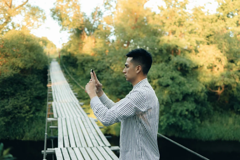 a man taking a picture of himself on a bridge, a picture, inspired by Ding Yunpeng, pexels contest winner, realism, holding a very advance phone, al fresco, standing sideways, hoang long ly