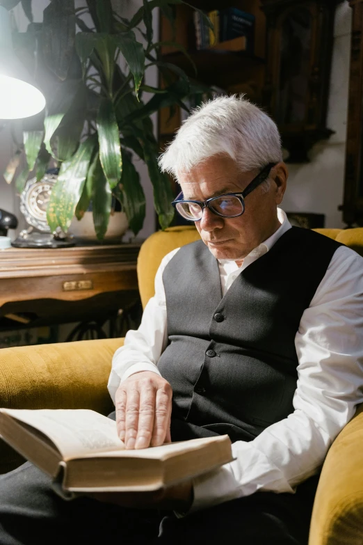 a man sitting in a chair reading a book, inspired by Carlo Maderna, medium length slick white hair, reading glasses, ignant, biopic