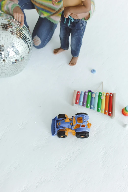 a woman and a child playing with a disco ball, white concrete floor, trucks, detailed product image, multi - coloured