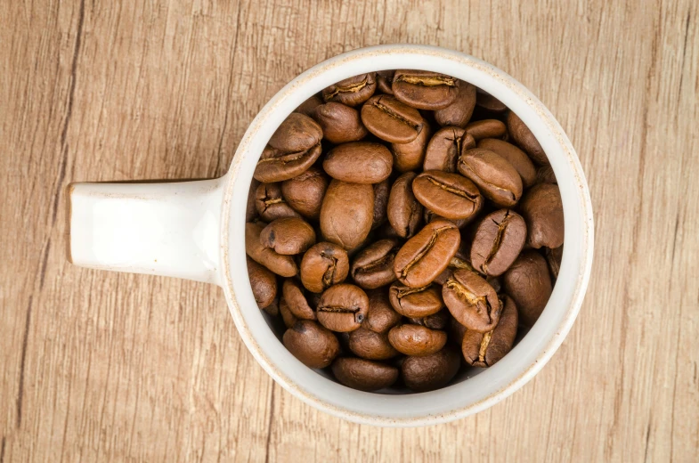 a cup filled with coffee beans on top of a wooden table, jen atkin, highly upvoted, thumbnail, high-resolution photo