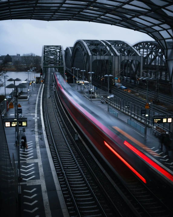 a train traveling down train tracks next to a train station, by Kristian Zahrtmann, pexels contest winner, on a bridge, lgbtq, lower saxony, 🚿🗝📝