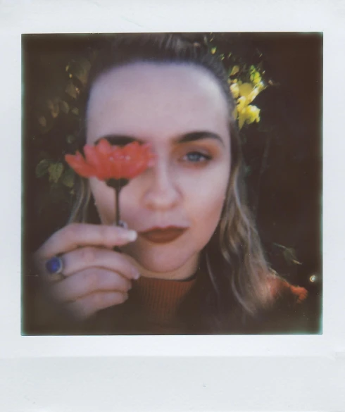 a woman holding a flower in front of her face, a polaroid photo, unsplash, florence pugh, 256435456k film, ((portrait)), 50mm photo