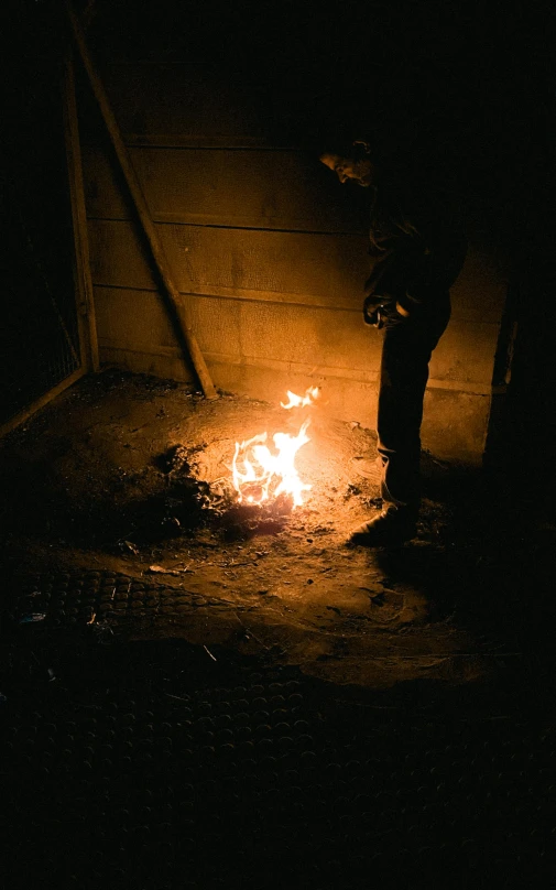 a person standing next to a fire in the dark, in an arena pit, inside a shed, profile image, maintenance photo