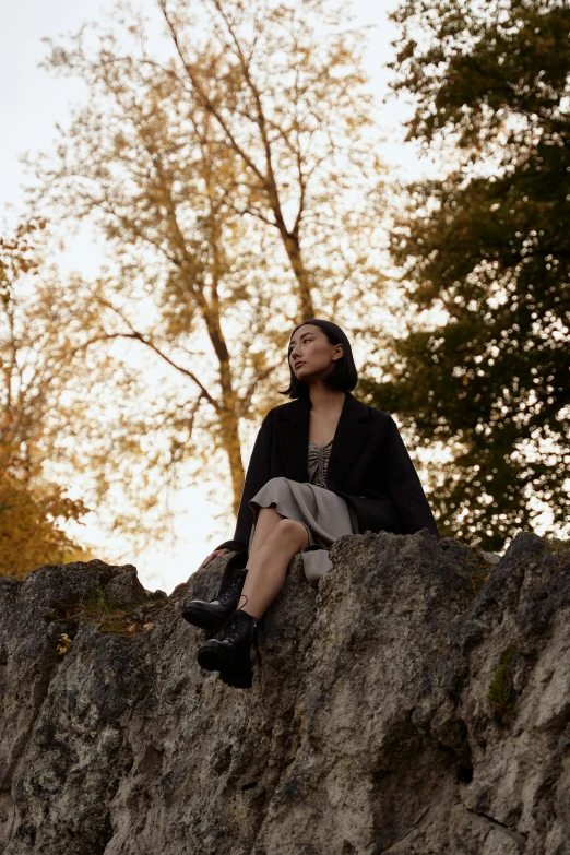 a woman sitting on top of a large rock, wearing black overcoat, sitting on a leaf, instagram picture, taken with sony alpha 9
