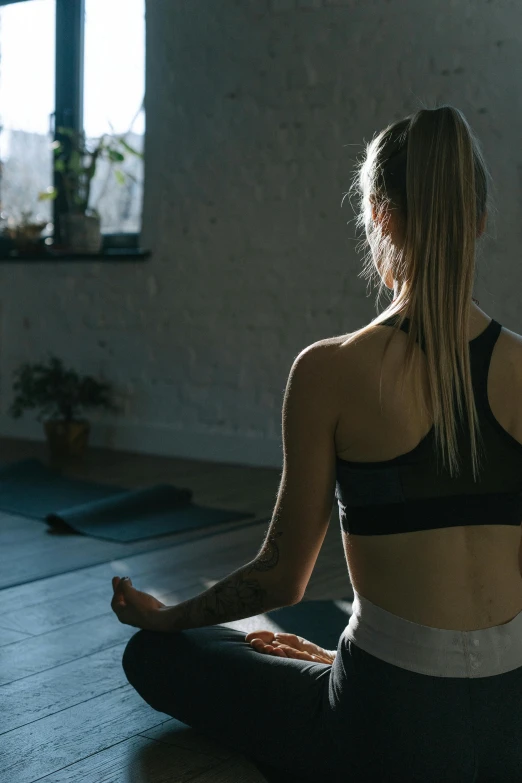 a woman sitting in the middle of a yoga pose, trending on pexels, light and space, focus her back, low light cinematic, sports clothing, spa