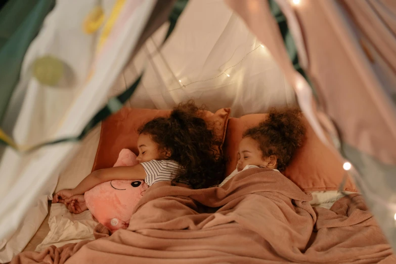 a couple of kids laying on top of a bed, pexels contest winner, brown and pink color scheme, interior of a tent, ( ( dark skin ) ), squishmallow