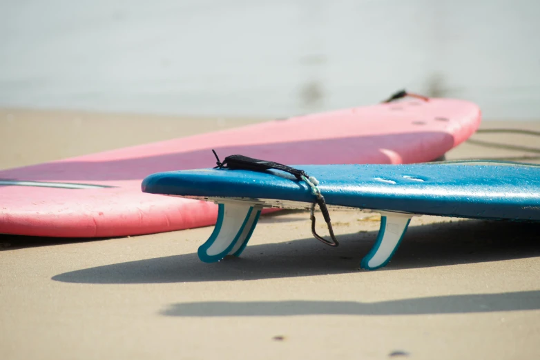 a couple of surfboards sitting on top of a sandy beach, pink and blue, neoprene, zoomed in, long fingers