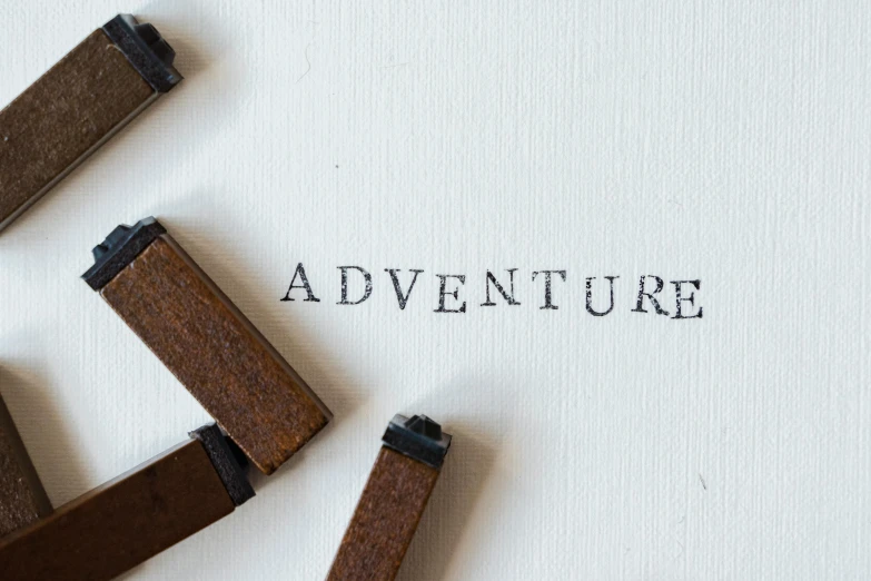 a piece of paper with the word adventure written on it, inspired by Salomon van Abbé, pexels contest winner, wooden art toys, stamp, alessio albi, story art