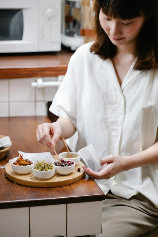 a woman sitting at a table with a plate of food, inspired by Cui Bai, trending on pexels, lab coat and tee shirt, on a wooden tray, pot, white sleeves