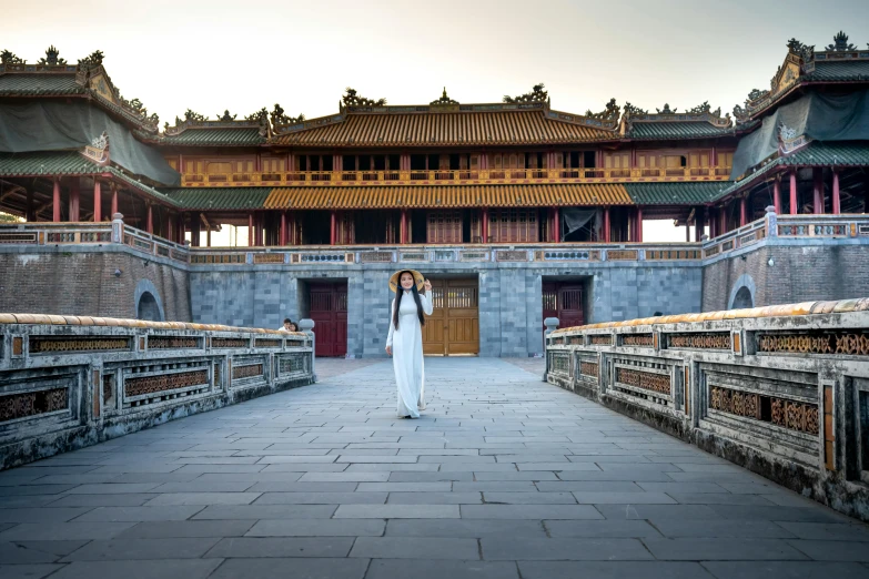 a woman standing in front of a building, inspired by Gu An, pexels contest winner, royal palace, with walkways, square, ao dai