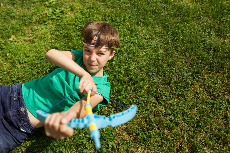 a young boy laying on top of a lush green field, by Sebastian Spreng, pexels contest winner, wielding a decorated halberd, toy photo, crossbow, casual playrix games