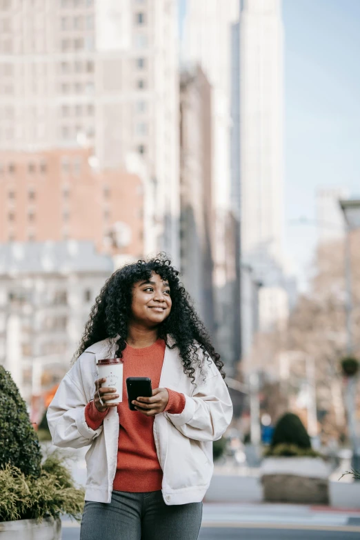 a woman walking down the street looking at her cell phone, trending on pexels, happening, brown curly hair, square, nyc, delightful surroundings