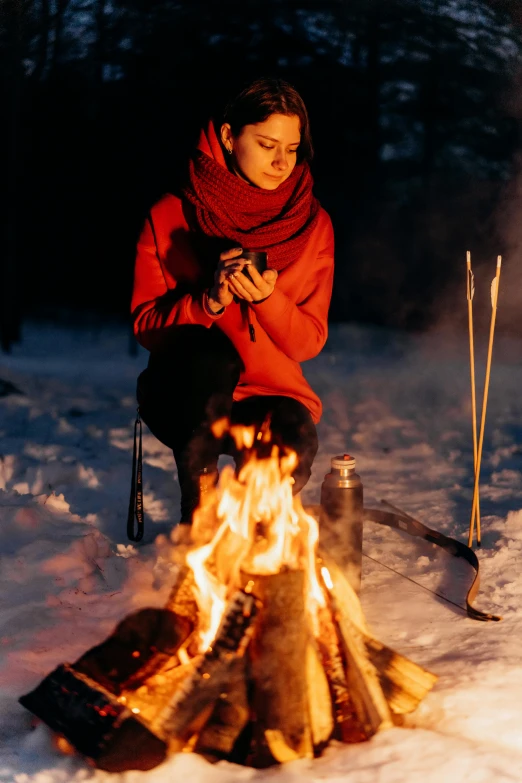 a woman sitting next to a fire in the snow, checking her phone, standing in fire, wearing adventure gear, rituals
