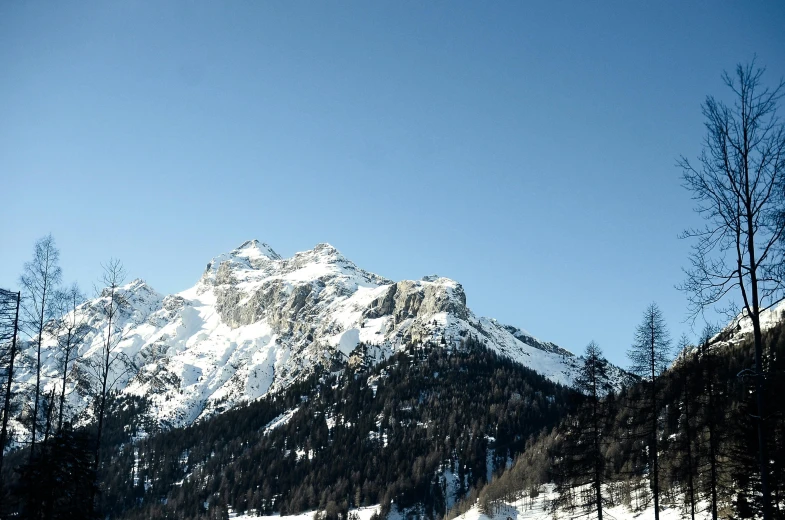 a group of people riding skis down a snow covered slope, a picture, les nabis, giant imposing mountain, thumbnail, clear blue skies, landscape photo