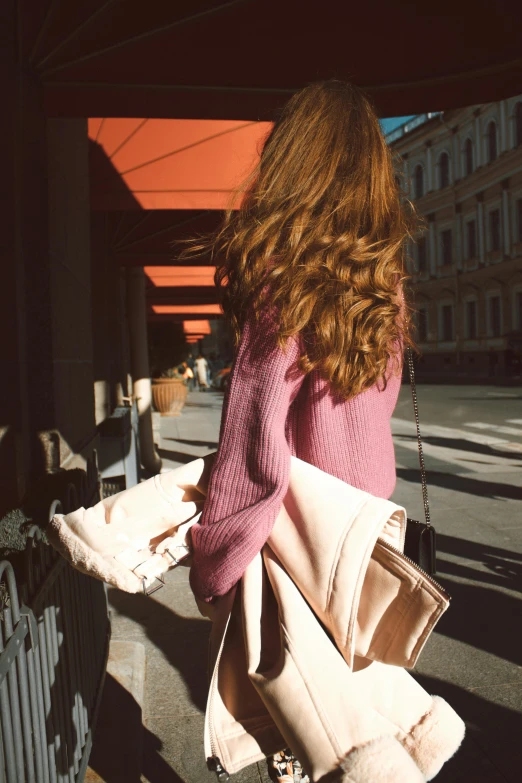 a woman walking down a sidewalk carrying a purse, a picture, by Anita Malfatti, trending on pexels, pink hue, her loose hair, seen from behind, warm cosy colors