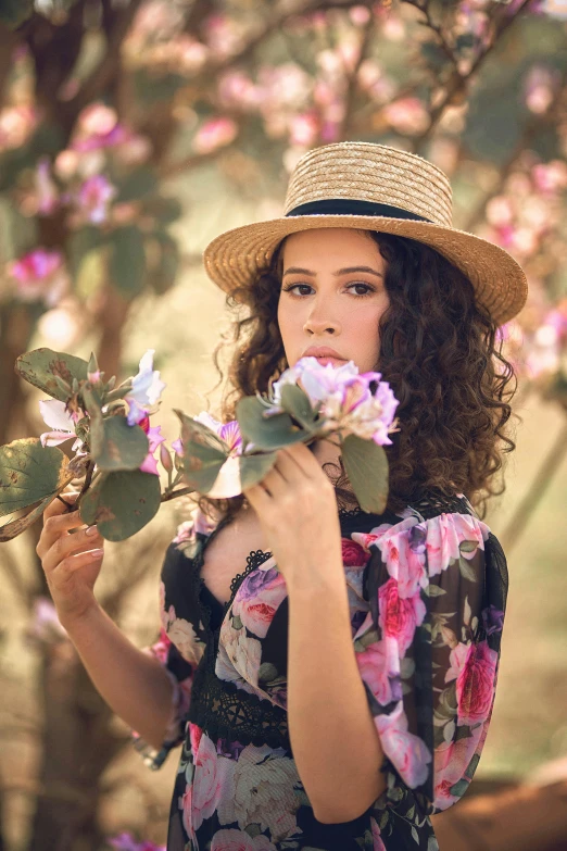 a woman in a hat holding a bunch of flowers, a portrait, pexels contest winner, curly haired, young southern woman, pink flowers, flowers and trees