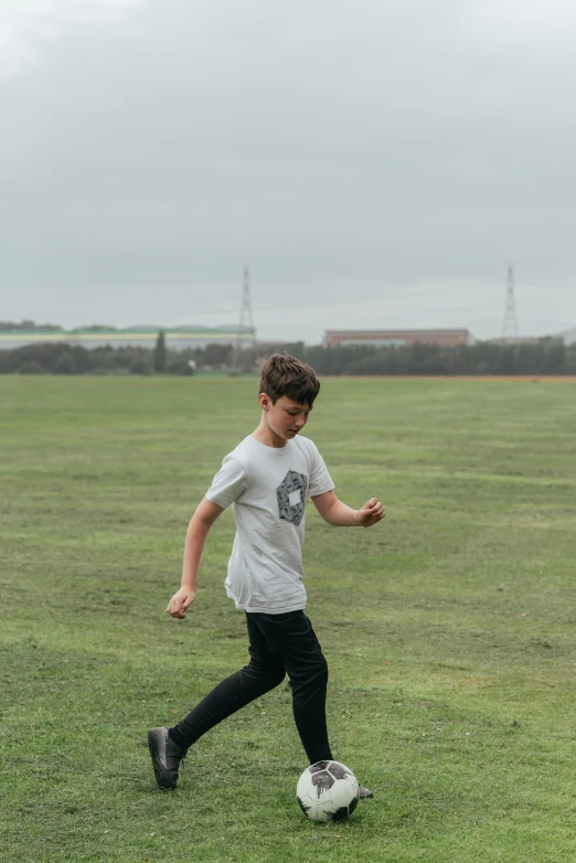 a young boy kicking a soccer ball on a field, an album cover, unsplash, happening, walking boy, casually dressed, on a cloudy day, low quality video