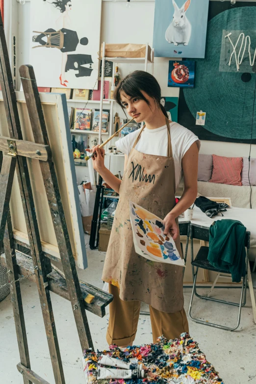 a woman that is standing in front of a easel, wearing an apron, canvas art