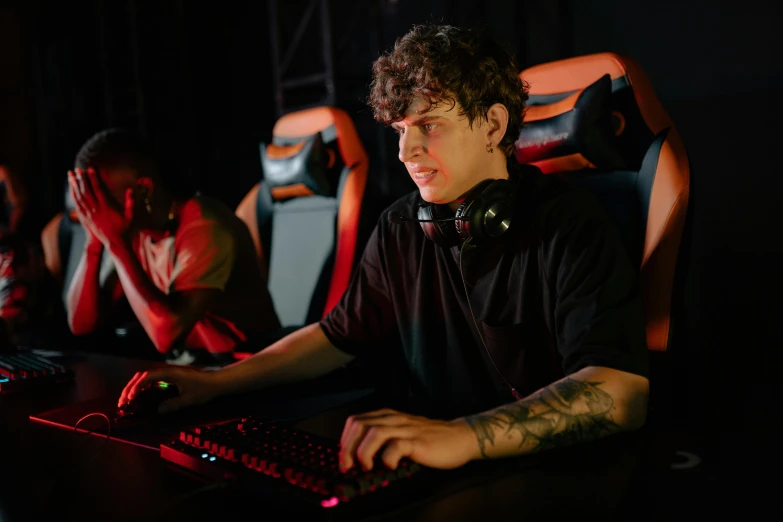 a man sitting at a desk in front of a computer, pexels, realism, e-sport style, medium shot of two characters, model is wearing techtical vest, declan mckenna