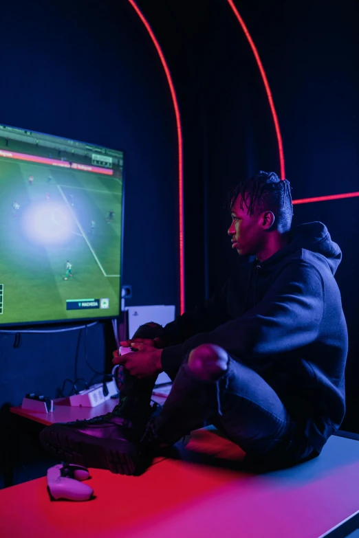 a man sitting on top of a table in front of a computer, playing soccer, playboi carti, control the game, dark setting