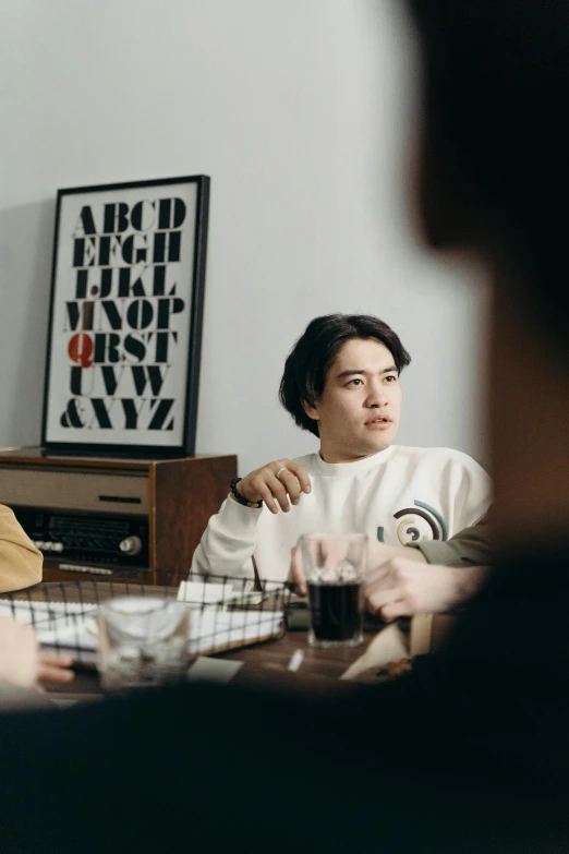 a group of people sitting around a table, poster art, by Jang Seung-eop, pexels contest winner, he is wearing a brown sweater, at home, typographic, portrait mode photo