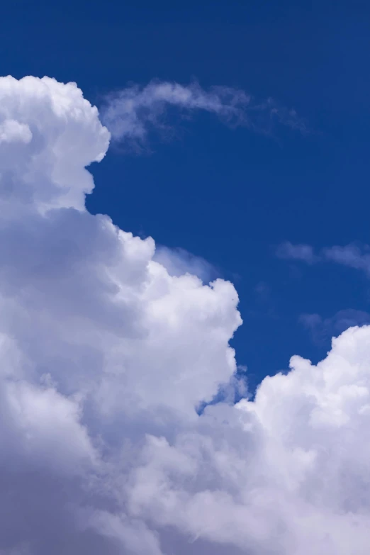 a plane flying through a cloudy blue sky, by Peter Churcher, towering cumulonimbus clouds, “puffy cloudscape, photograph, long