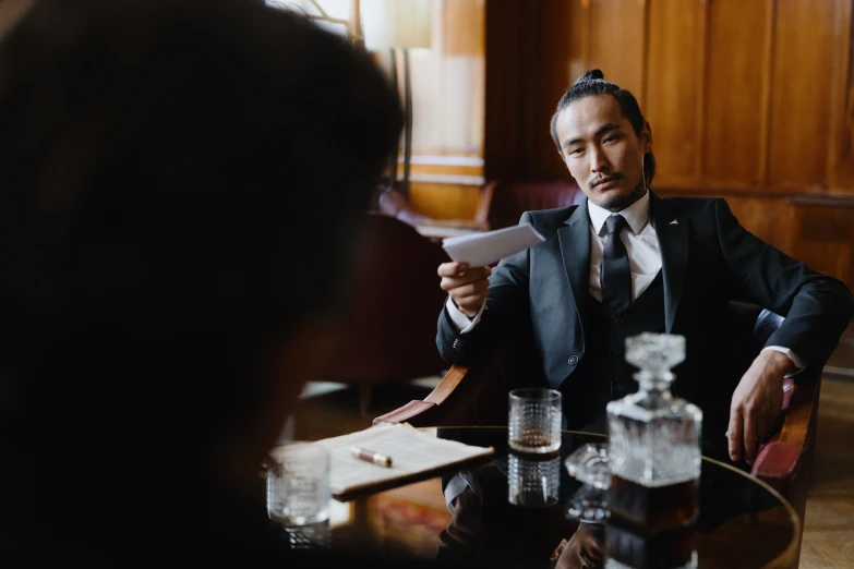 a man in a suit sitting at a table, pexels contest winner, holding court, speakeasy, asian male, thumbnail