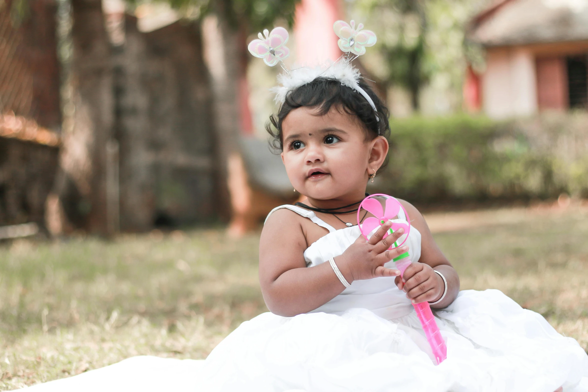 a little girl that is sitting in the grass, pexels contest winner, jayison devadas, holding a bow, white and pink cloth, wearing a fancy dress