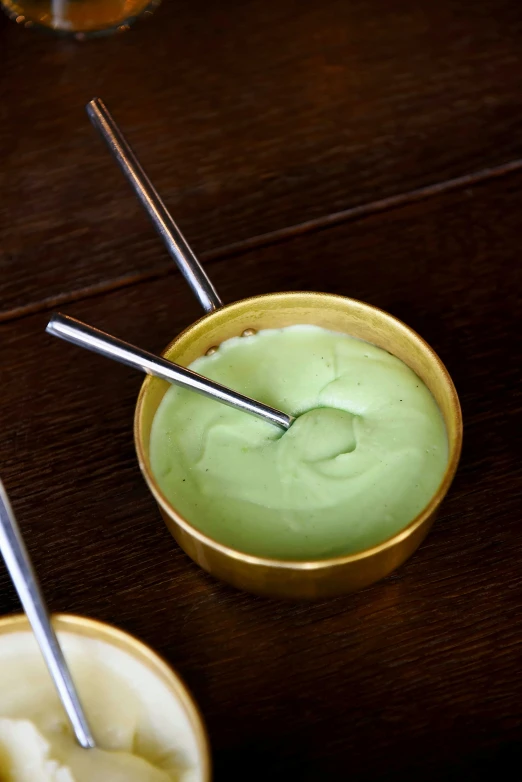 a wooden table topped with two bowls of dips, a portrait, inspired by Kanō Shōsenin, unsplash, pastel green, ice cream, metalic green, close - up photograph