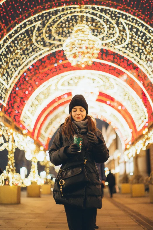 a woman standing in the middle of a walkway covered in christmas lights, a picture, drinking, moscow, profile image, guide