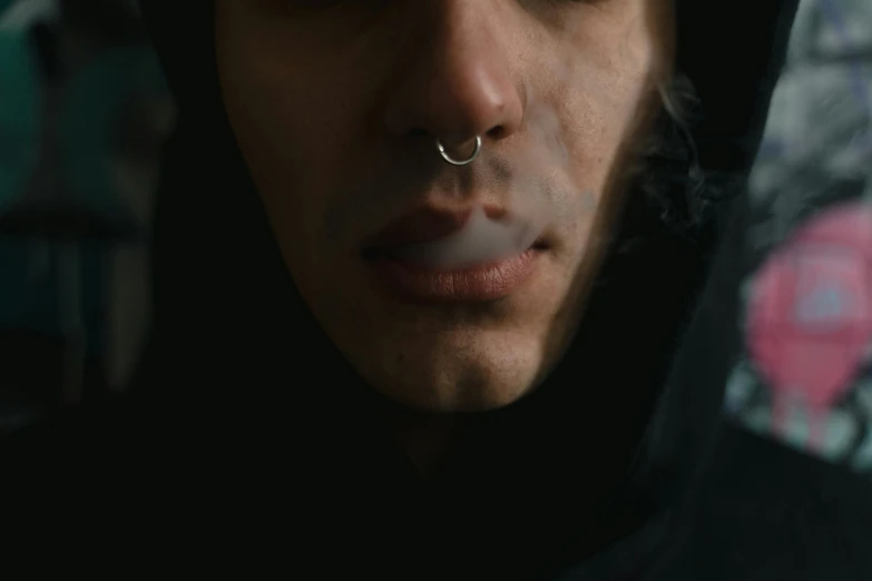 a man in a hoodie smoking a cigarette, a character portrait, trending on pexels, symmetrical face orelsan, 2 0 2 1 cinematic 4 k framegrab, septum piercing, high angle close up shot
