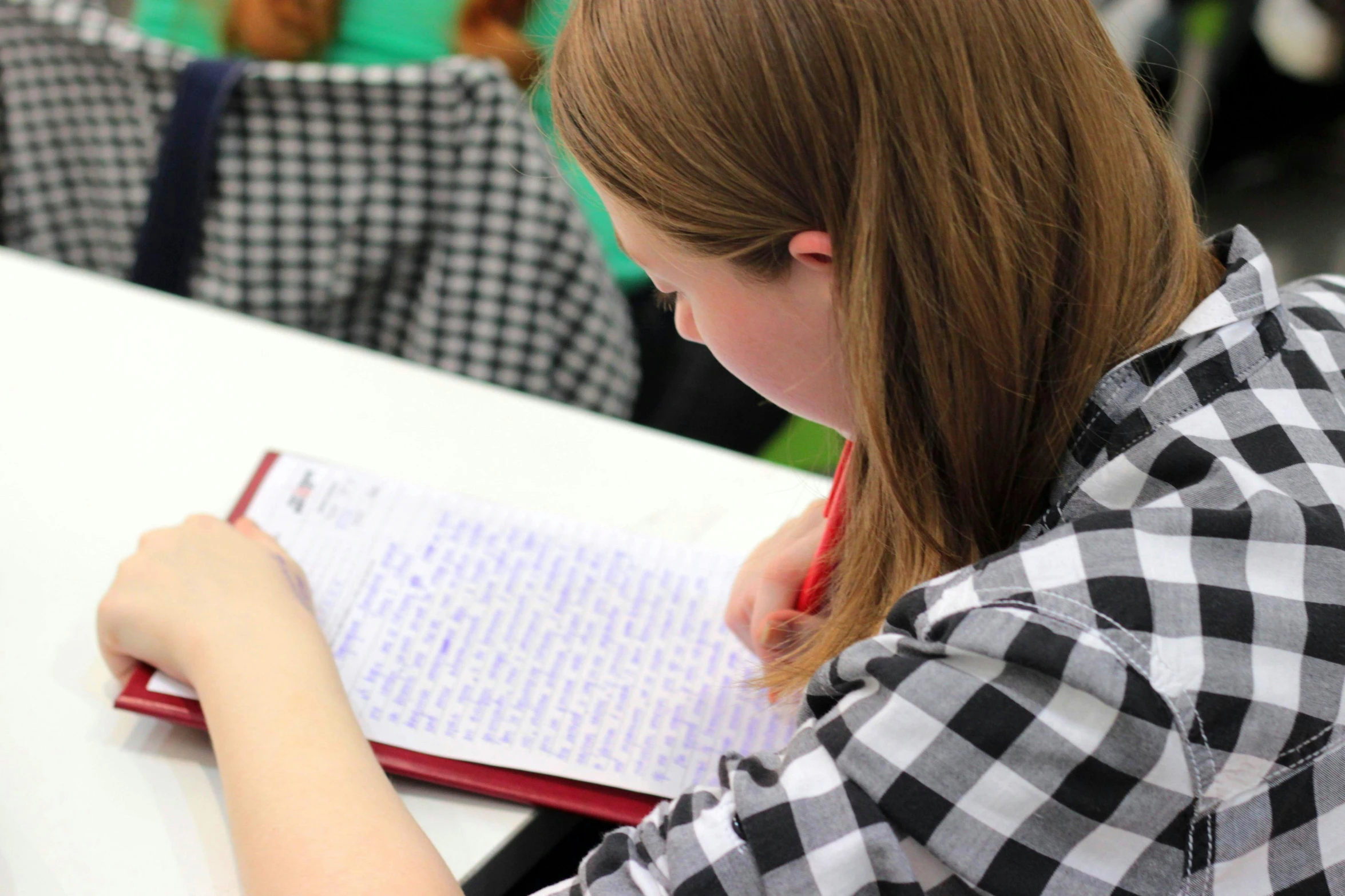 a woman sitting at a table writing on a piece of paper, pexels contest winner, academic art, red writing, background image, school class, taken in the late 2010s