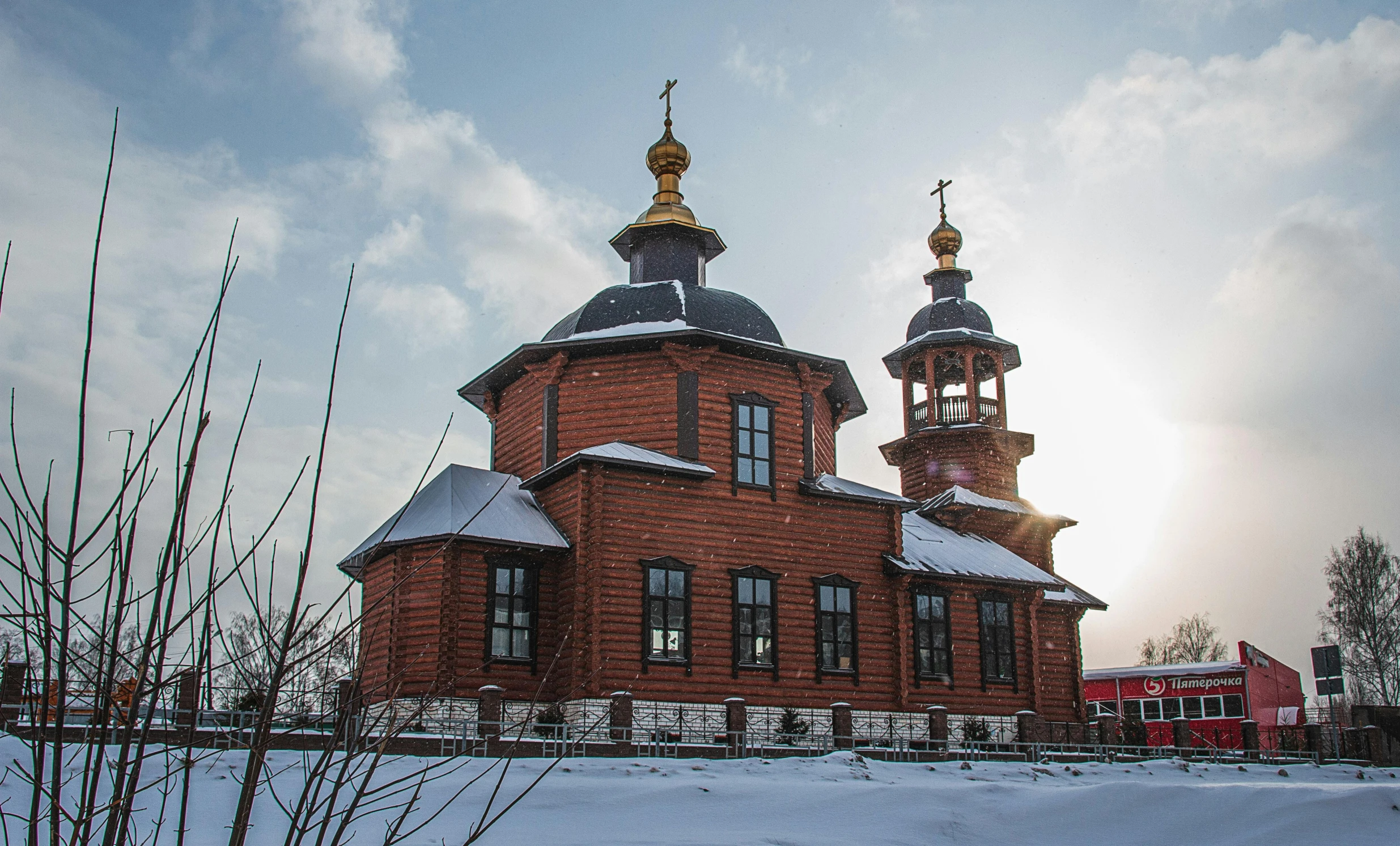 a large red building sitting in the middle of a snow covered field, orthodox icons, black domes and spires, wooden buildings, exterior photo