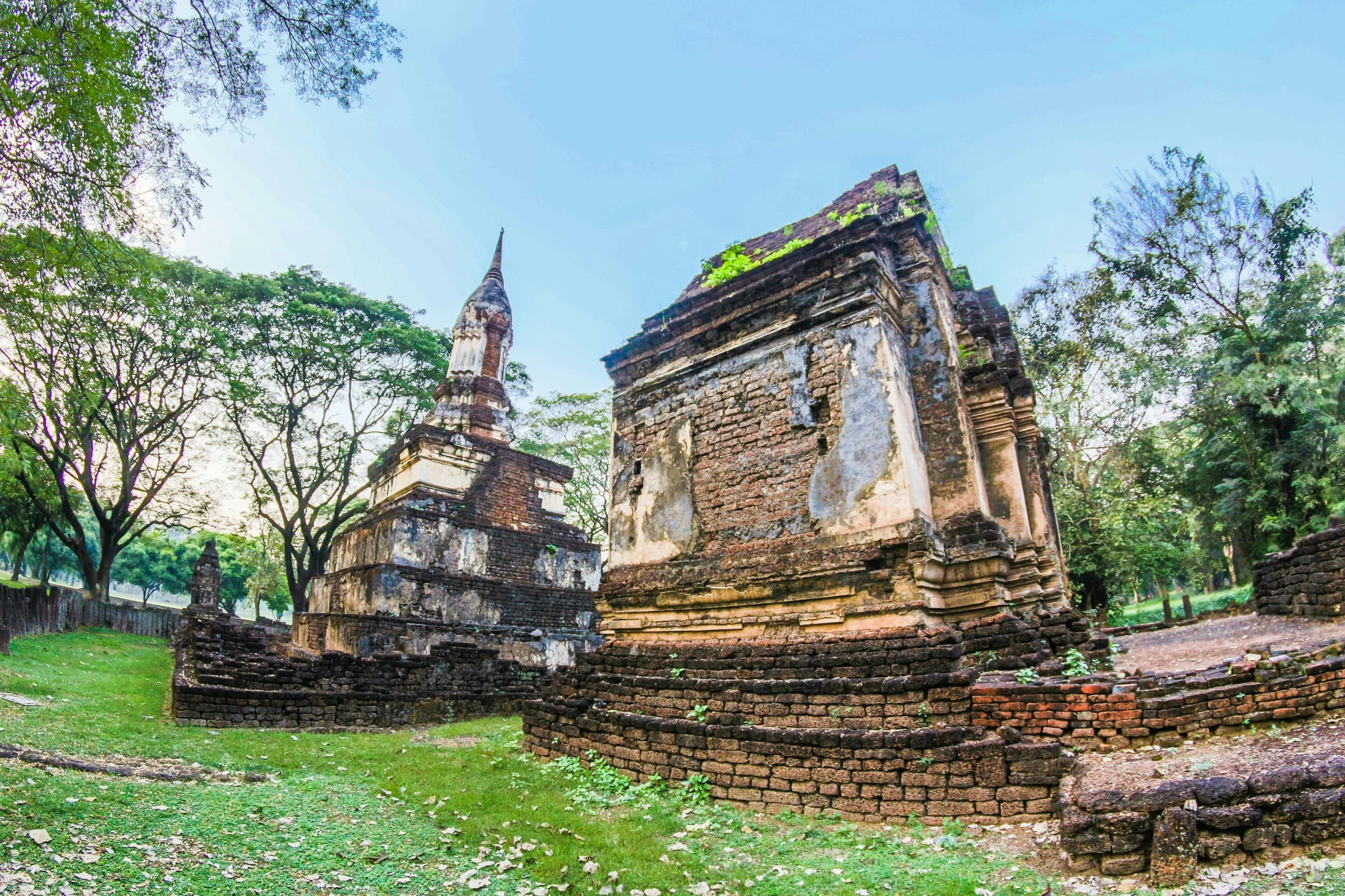 a group of buildings sitting on top of a lush green field, graffiti, sukhothai costume, ornate city ruins, background image, wide angle”