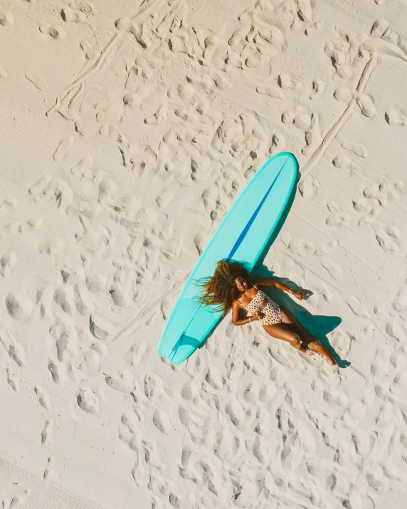 a woman laying on a beach with a surfboard, by Carey Morris, pexels contest winner, minimalism, aerial footage, thumbnail, teal skin, light tan