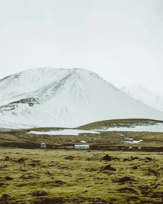 a grassy field with a mountain in the background, by Hallsteinn Sigurðsson, pexels contest winner, land art, snowing, background image, 90's photo, on a desolate plain