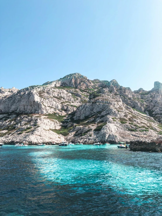 a body of water with a mountain in the background, a photo, les nabis, over a calanque, thumbnail, light blue water, rocky cliffs