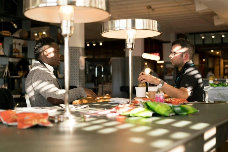 a couple of men sitting at a table with food, profile image, brightly lit, darren bartley, customers