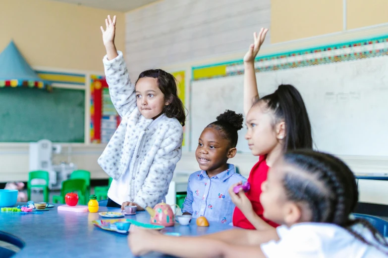 a group of children sitting at a table in a classroom, by Arabella Rankin, pexels contest winner, waving arms, model posing, advert, promotional image