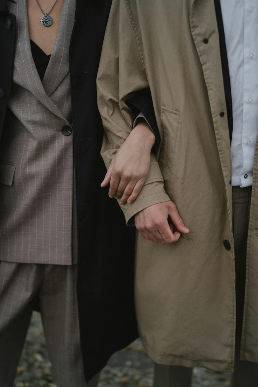 a couple of people standing next to each other, trending on pexels, trench coat and suit, human bodies intertwined, muted arm colors, androgynous person