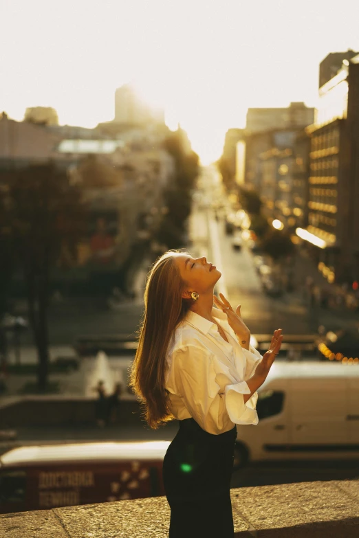 a woman standing on a sidewalk looking up at the sky, trending on pexels, flowing backlit hair, wearing a white button up shirt, city rooftop, hot with shining sun