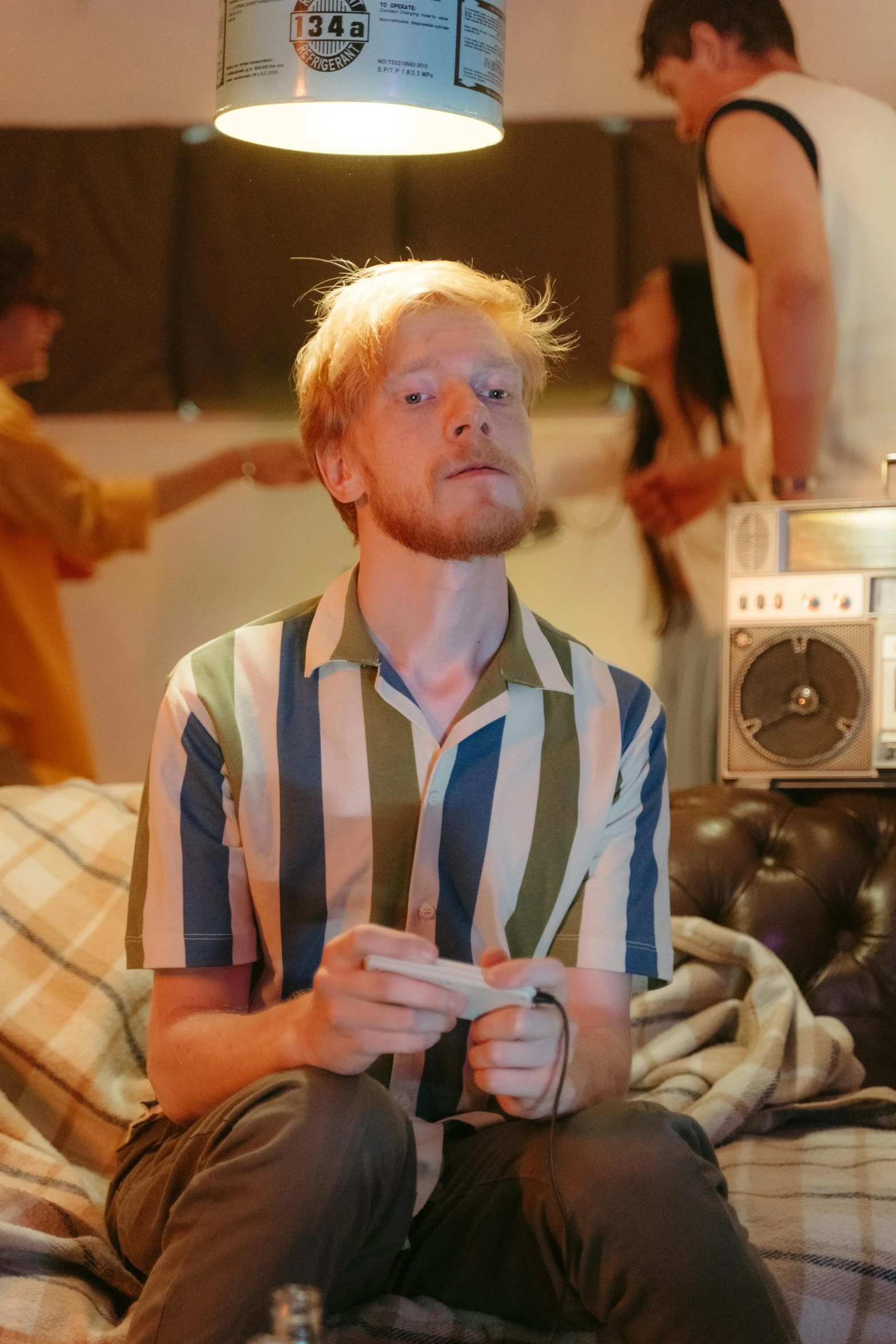 a man sitting on a couch playing a video game, an album cover, trending on reddit, photorealism, ginger hair with freckles, performing a music video, still from a wes anderson movie, standing in a dimly lit room