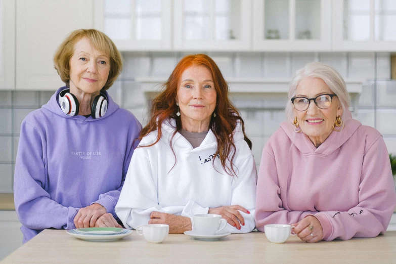 three women sitting at a table with cups of coffee, a portrait, trending on pexels, antipodeans, wearing an oversized hoodie, elderly, molly weasley, posing together in bra