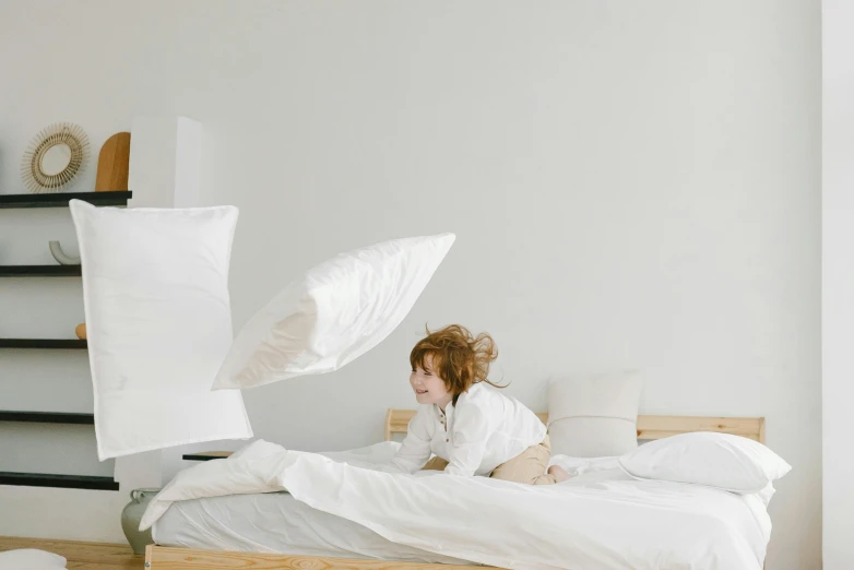 a woman sitting on top of a bed with pillows, pexels contest winner, little kid, minimalistic design, majestic sweeping action, white