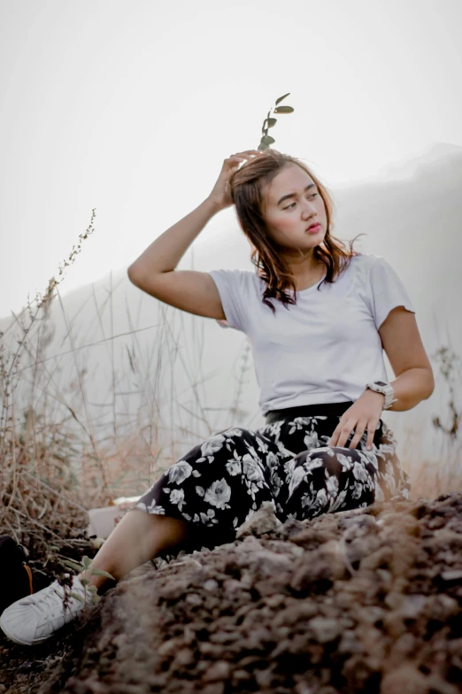 a woman sitting on top of a pile of dirt, inspired by Ruth Jên, pexels contest winner, wearing pants and a t-shirt, floral, distant thoughtful look, young himalayan woman