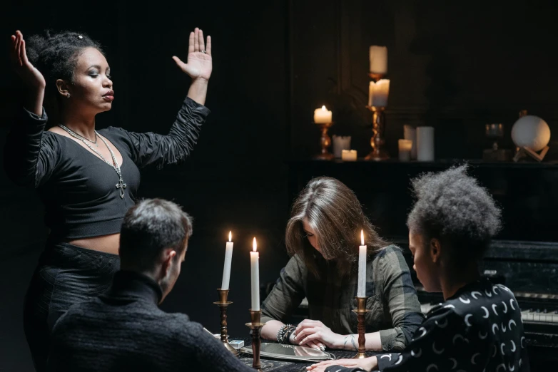 a group of people sitting around a table with candles, female occultist, back of hand on the table, promo image, photo of a black woman