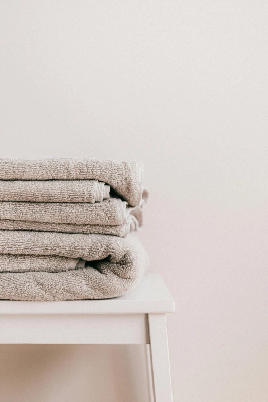 a stack of towels sitting on top of a white table, trending on pexels, ✨🕌🌙, taupe, softly - lit, wearing a simple robe