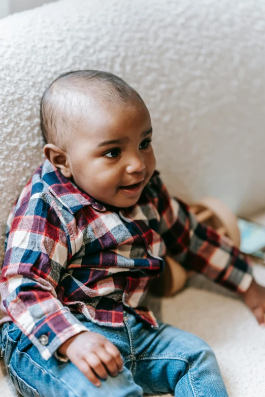 a baby sitting on top of a white chair, inspired by Myles Birket Foster, pexels contest winner, brown skin man with a giant grin, on a checkered floor, sitting in a waiting room, brown buzzcut