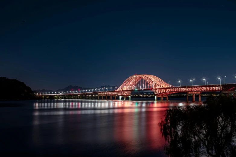 a bridge over a body of water at night, by Jang Seung-eop, pexels contest winner, red trusses, pyongyang city, view from the side, red and blue back light