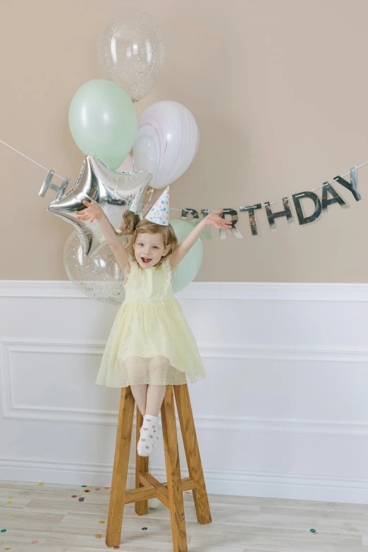a little girl standing on a stool holding a bunch of balloons, by Pamela Drew, pexels, wearing a light grey crown, happy friend, 🍸🍋, silver and yellow color scheme